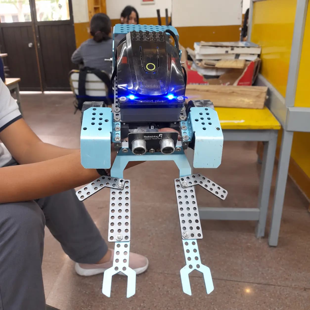 Un alumno sostiene un robot armado en el aula